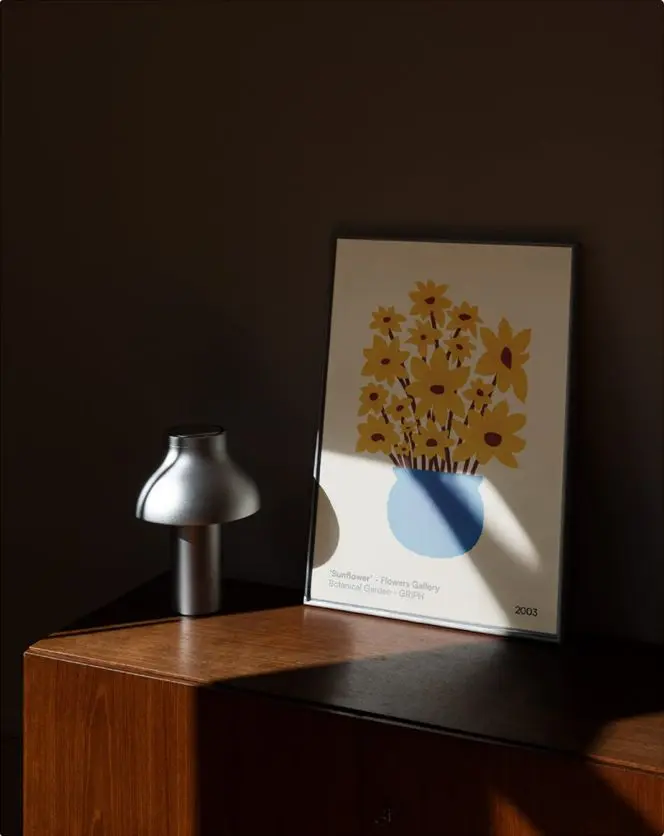 Une affiche de fleurs jaunes sur une commode, à côté d'une lampe.