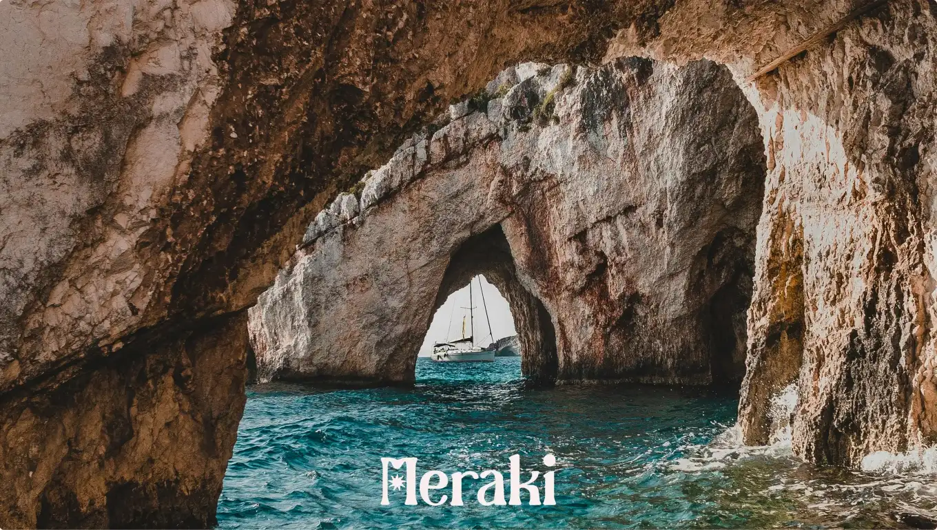 Une arche de roche au-dessus de la mer, un voilier au loin, et le logo Meraki.