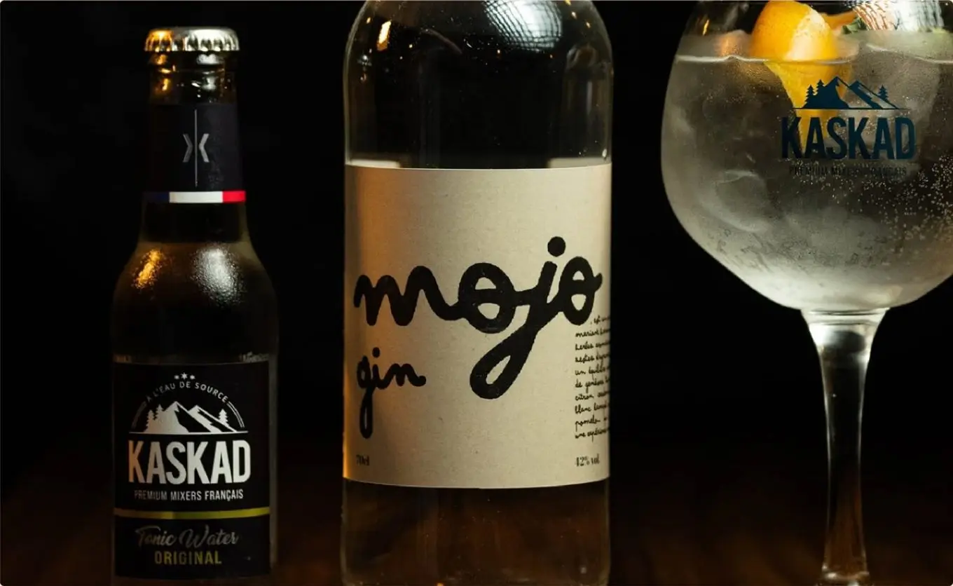 Une bouteille de Mojo gin entre un tonic Kaskad et un verre de gin tonic.